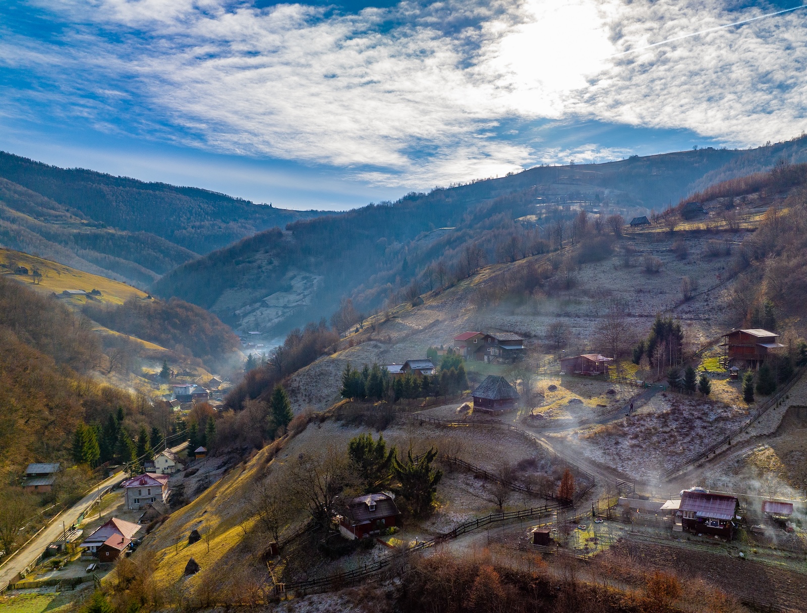 Sat montan luminat de soare, cu ceață ușoară pe vale